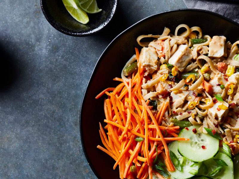 Pad Thai with Tofu sprinkeld with carrots and cucumbers in a large black bowl