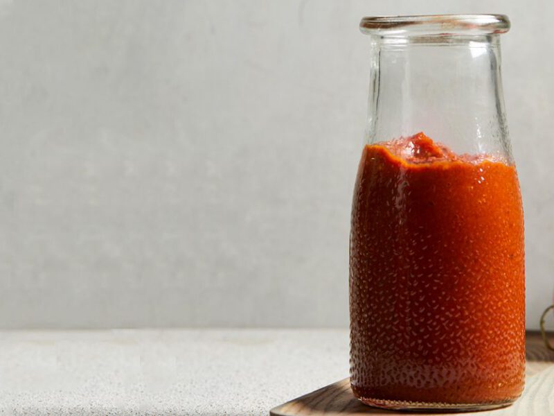 Homemade Ketchup in a glass bottle sitting on a wood cutting board next to fresh tomatoes