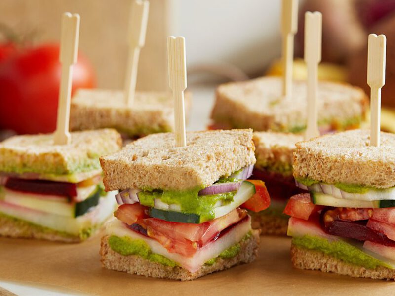 Stacked veggie sandwiches on a cutting board with wood toothpicks holding them together