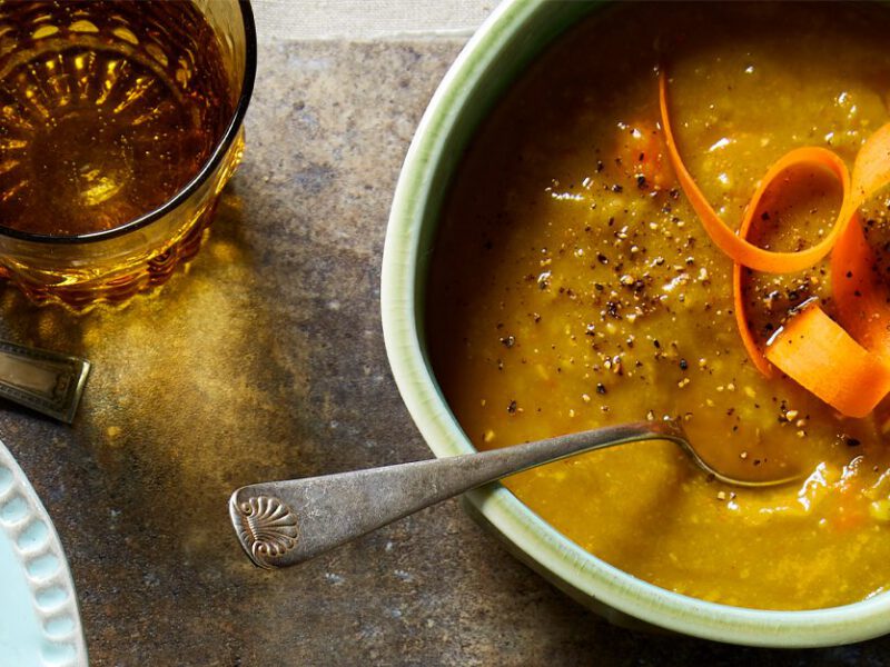 Slow-Cooker Split Pea Soup garnished with a carrot ribbon and celery leaves in a light blue bowl