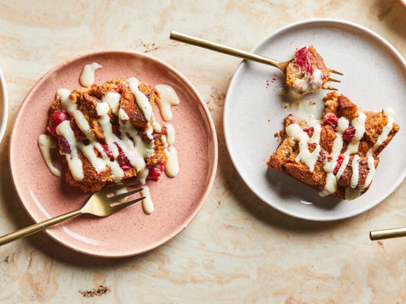 Cranberry-Orange Bread Pudding on white and pink plates drizzled with a creamy sauce