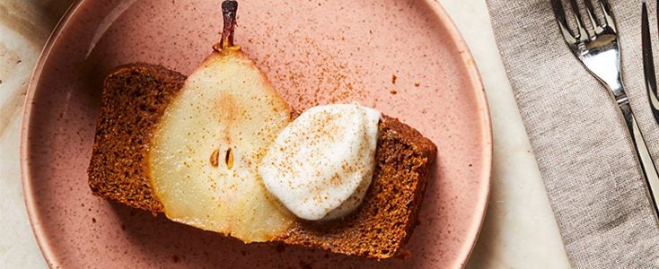 Slice of gingerbread cake with a slice of whole poached pear shown in the middle