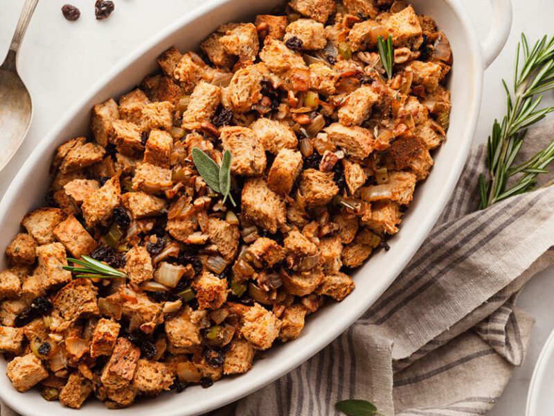 Vegan whole grain stuffing shown in white casserole dish, sprinkled with dried currants