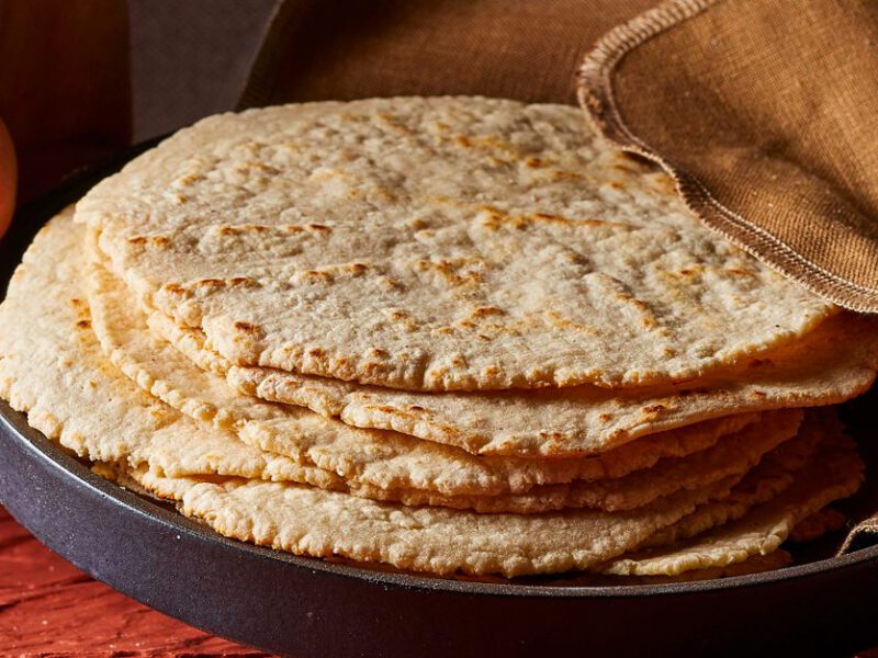 Hands holding a plate of stacked corn tortillas
