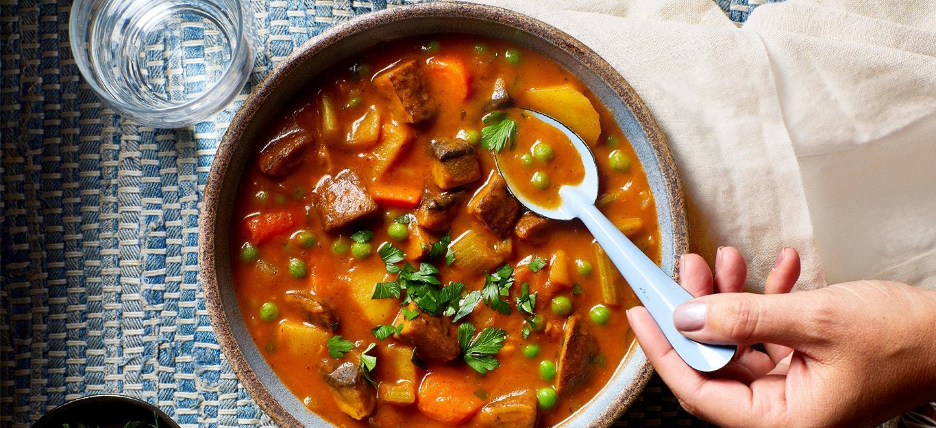 A woman's hand scoop up a spoonful of the Best-Ever Beefless Stew (a Vegan Beef Stew) from a ceramic bowl