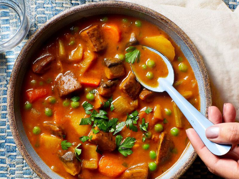 A woman's hand scoop up a spoonful of the Best-Ever Beefless Stew (a Vegan Beef Stew) from a ceramic bowl