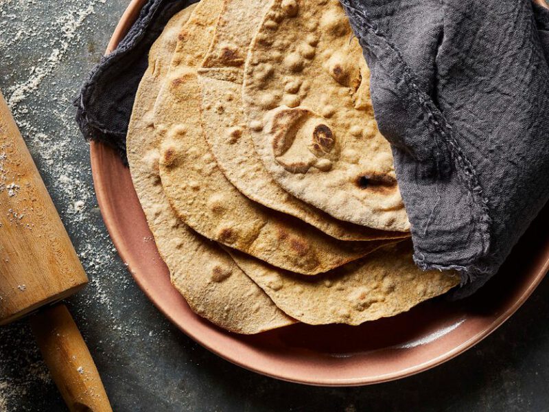 Whole Wheat Flour Tortillas on a pink plate next to a rolling pin sprinkled with flour