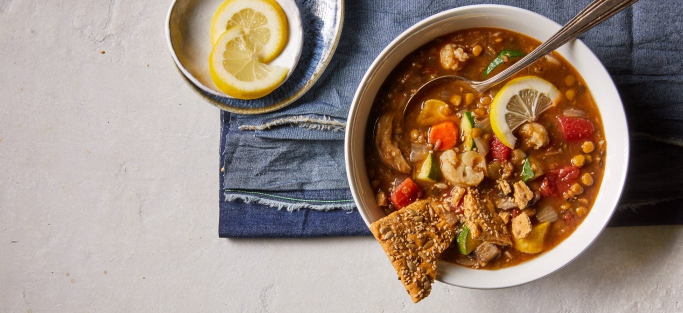 Clean-Your-Pantry Lentil-Vegetable Stew in a while bowl with crackers and lemon wedges