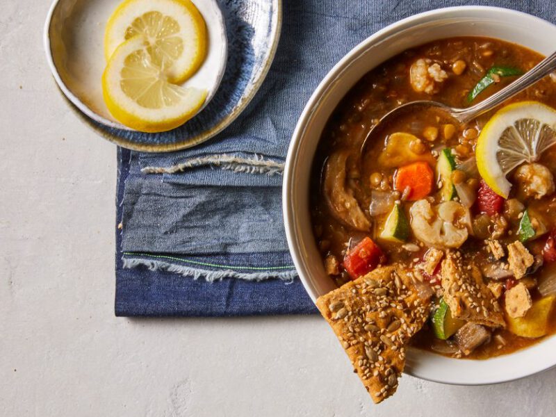 Clean-Your-Pantry Lentil-Vegetable Stew in a while bowl with crackers and lemon wedges