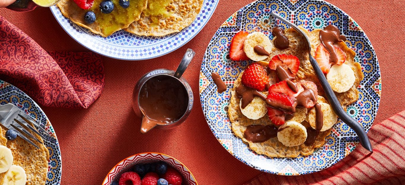 Sweet Moroccan Pancakes with Chocolate Banana Sauce and fresh fruit on a colorful plate and red tablecloth