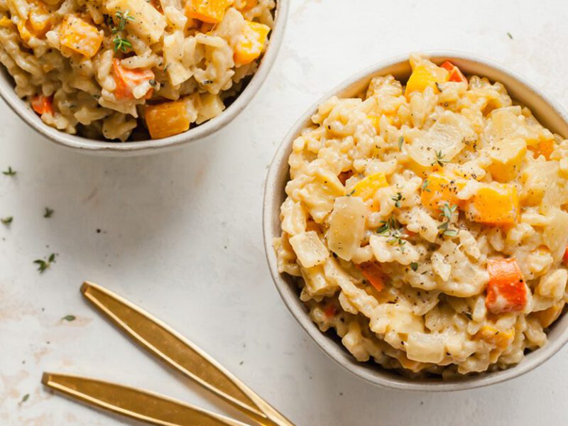 Two bowls of winter vegetable vegan risotto next to a small pot of fresh rosemary stalks
