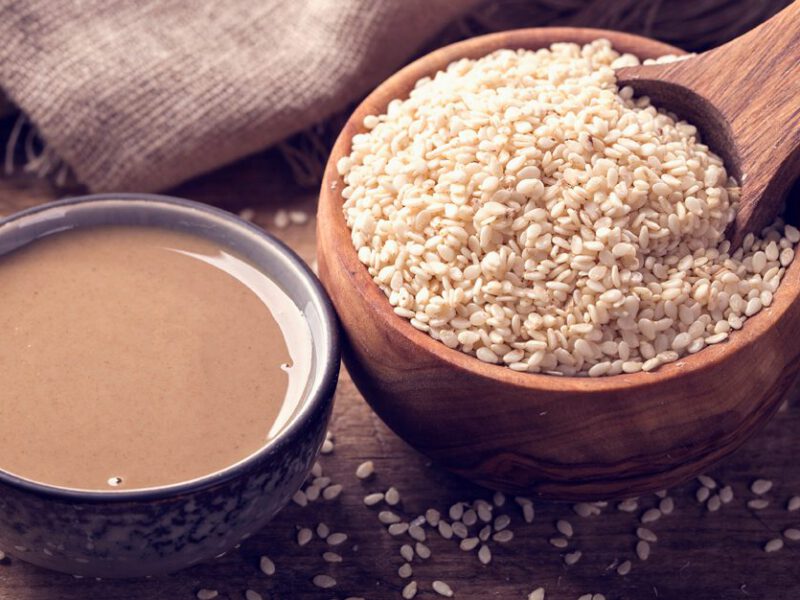 A small bowl of tahini next to a larger wooden bowl of sesame seeds.