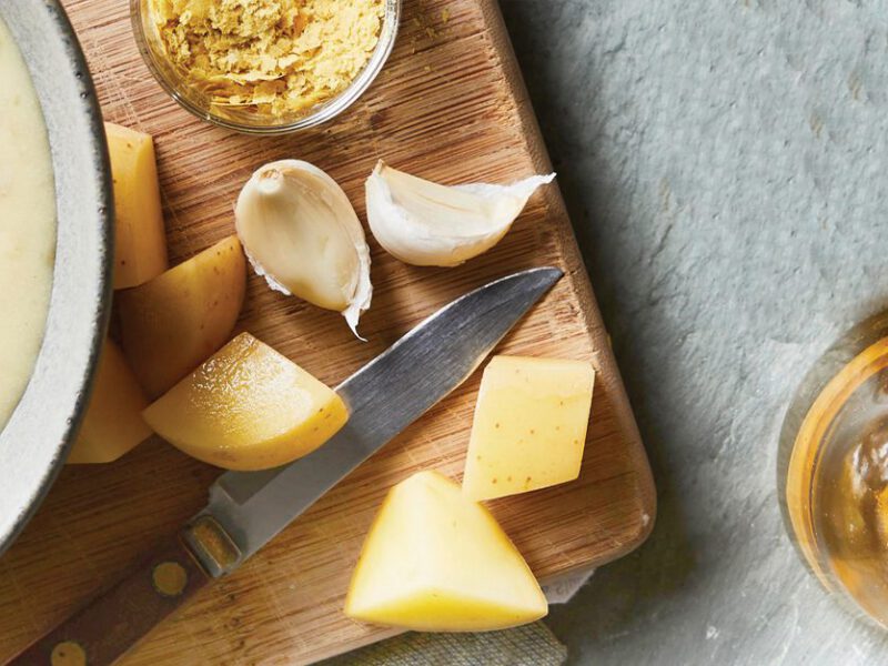 Vegan potato cheese sauce in a bowl surrounded by chunks of potato and garlic cloves