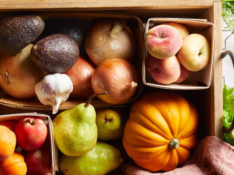 An assortment of fresh produce in a produce delivery box, including pumpkin, pears, peaches, potatoes