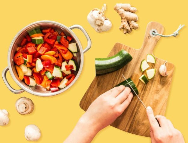 Hand chopping zucchini with a pot of chopped vegetables
