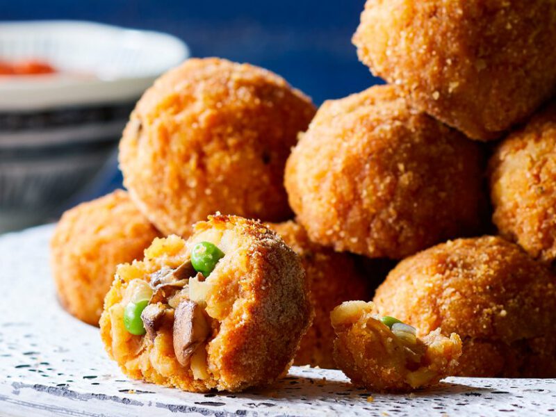 Sicilian Rice Balls with Mushrooms and Peas piled on a white platter with bowl of marinara sauce in background