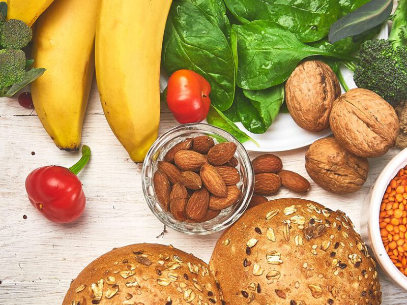 Vegetables, fruit, nuts, lentils and bread lay spread out on a white counter
