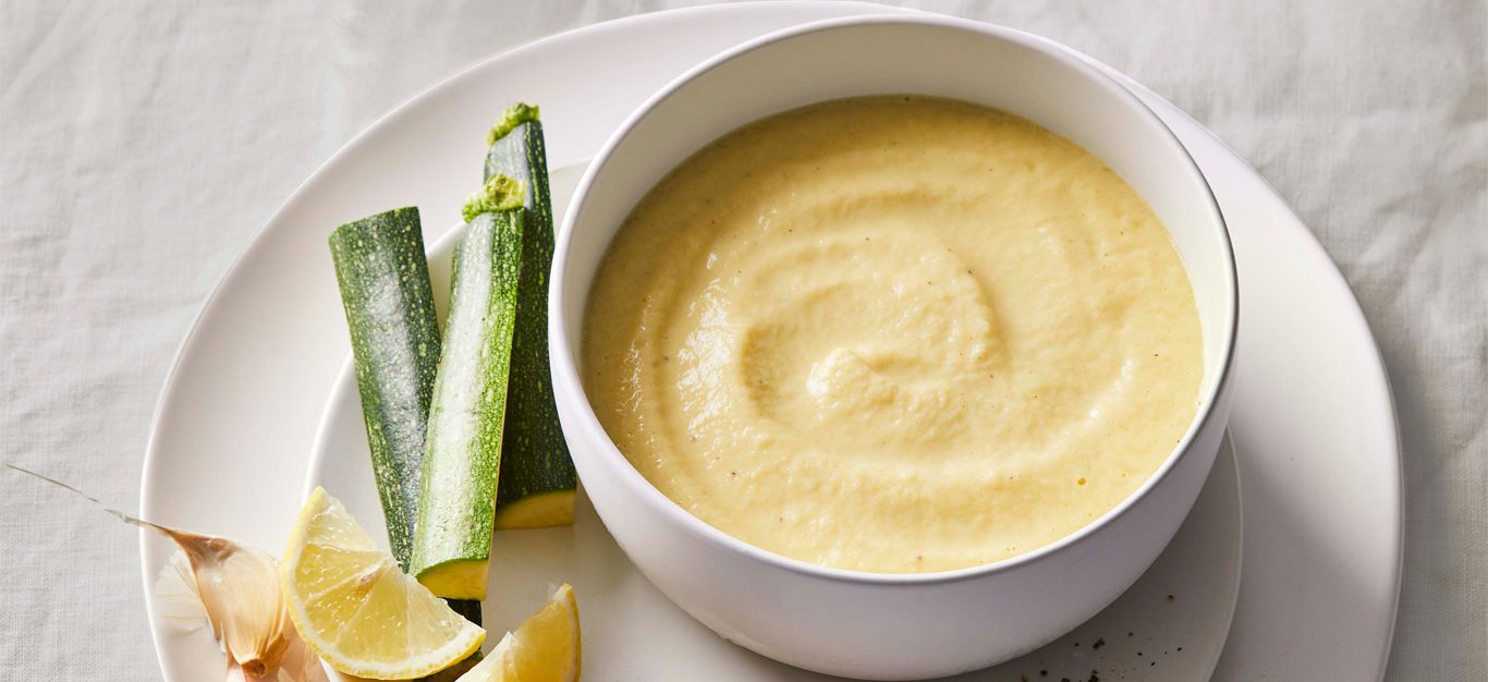 Low-Fat Tahini Dressing in a white bowl with sticks of zucchini on a white plate