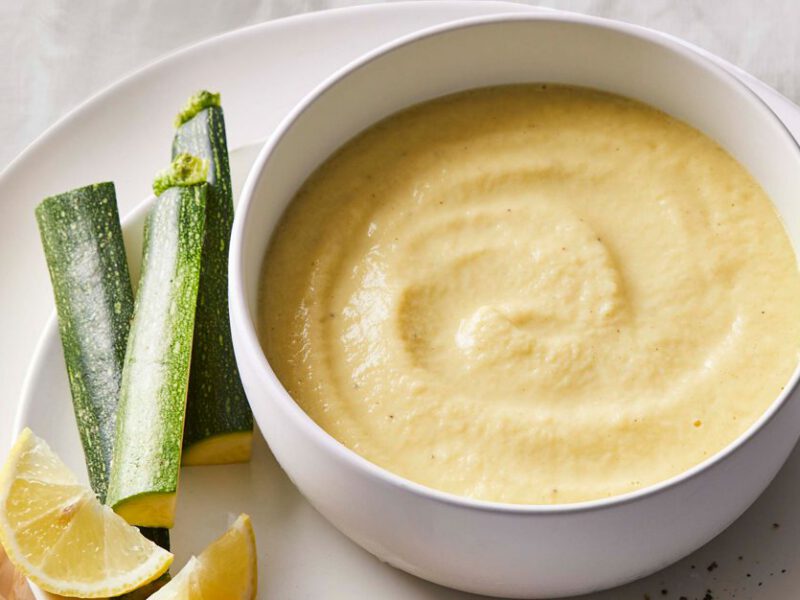 Low-Fat Tahini Dressing in a white bowl with sticks of zucchini on a white plate