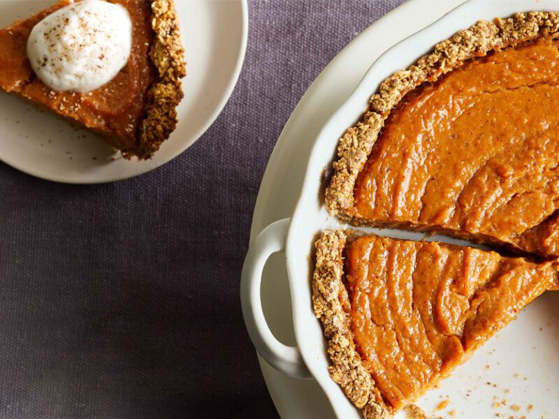 Vegan Sweet Potato Pie in a white pie tin with a slice topped with whipped cream sitting next to it on a saucer