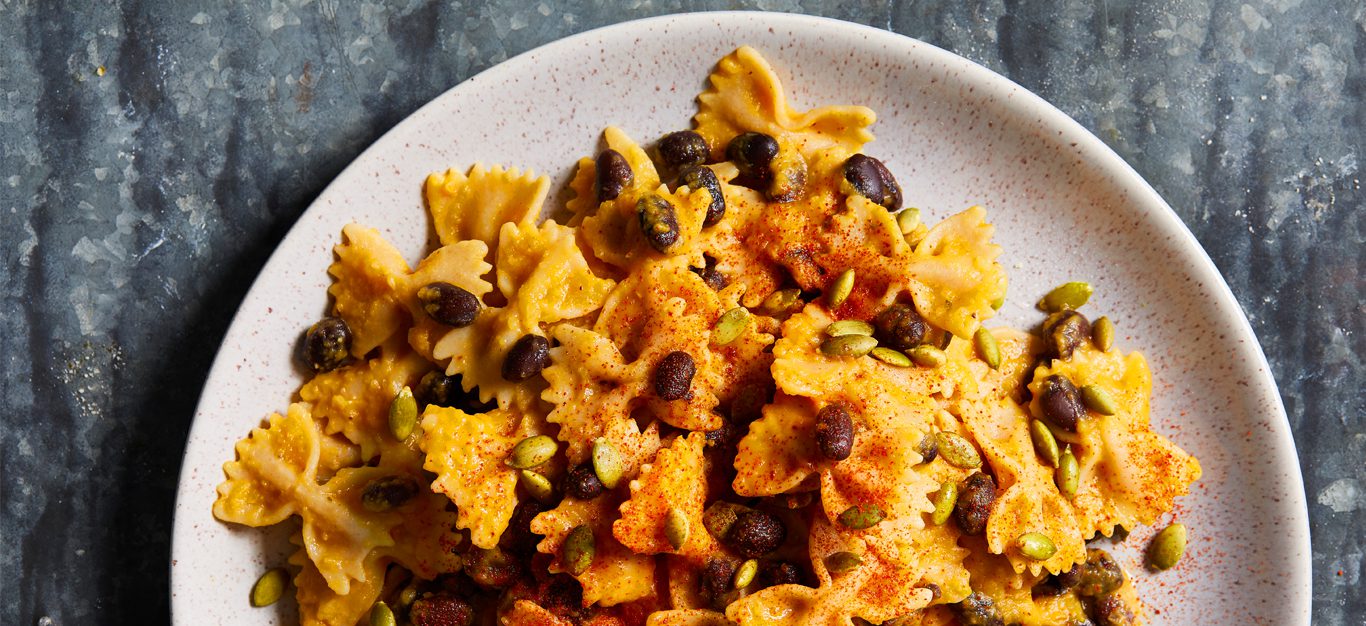 Butternut Cream Farfalle with Black Beans and Pumpkin Seeds on a white plate and gray background