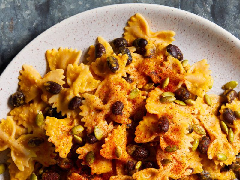Butternut Cream Farfalle with Black Beans and Pumpkin Seeds on a white plate and gray background