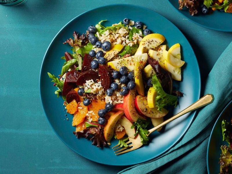 Eat-the-Rainbow Salad on a blue plate with metal fork on a teal tabletop