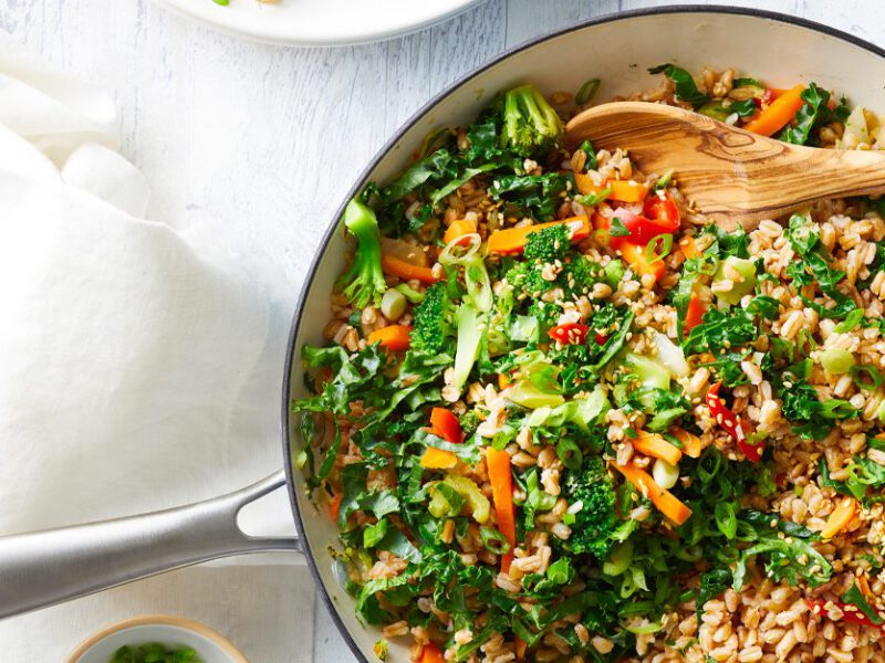 Oil-Free Farro Fried Rice in a white skillet with a wooden serving spoon