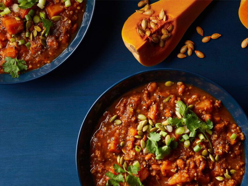 Butternut-Bulgur Chili in blue bowls with quartered butternut squash on the table next to the bowls