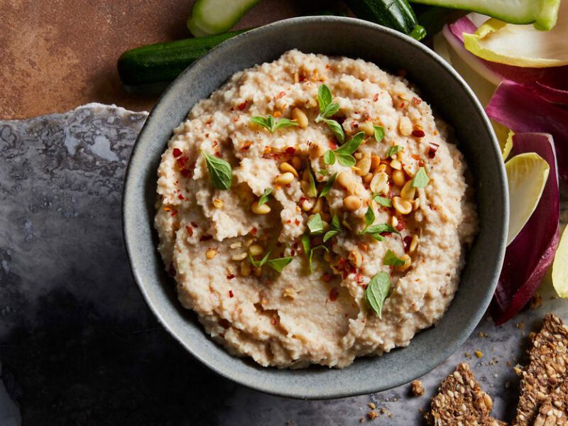 Roasted Cauliflower Hummus in a gray bowl surrounded by crackers and endive leaves