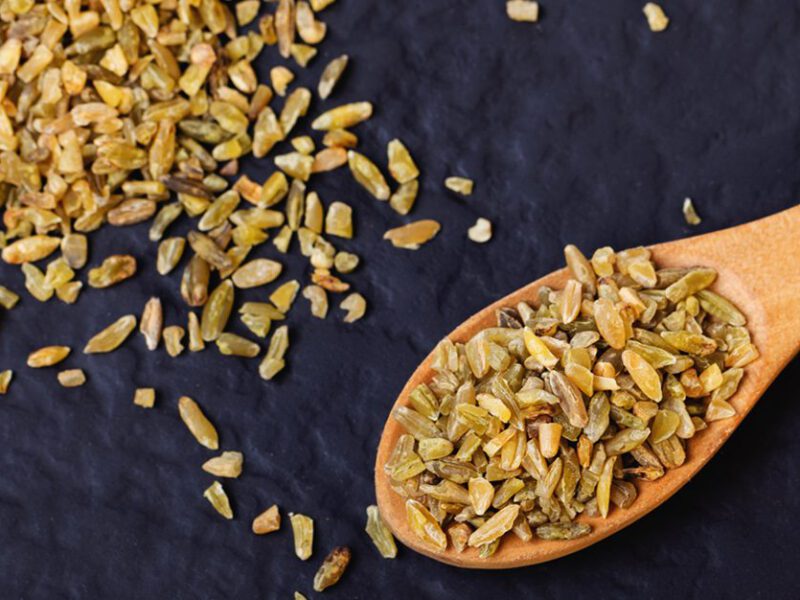 Freekeh grains in a wooden spoon and scattered across a black table
