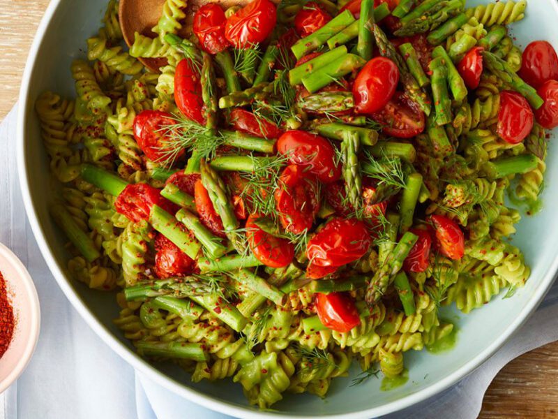 Creamy Avocado Kale Pasta in a white bowl on wooden table next to a small bowl of paprika