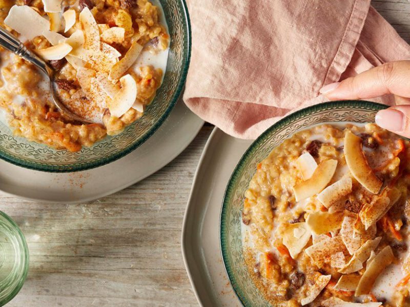 Tropical Slow-Cooker Oatmeal in blue glass bowls on a wooden table as a woman's hand reaches for one bowl
