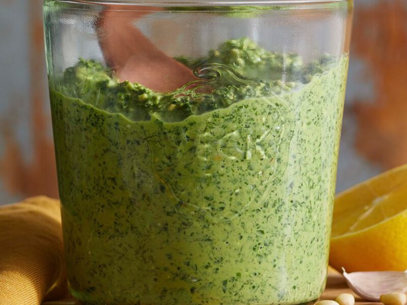 carrot top pesto in a glass jar next to a sliced lemon