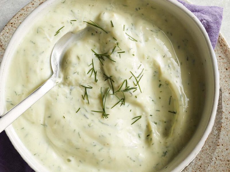 creamy dill dip in a white bowl with a metal spoon resting in the dip