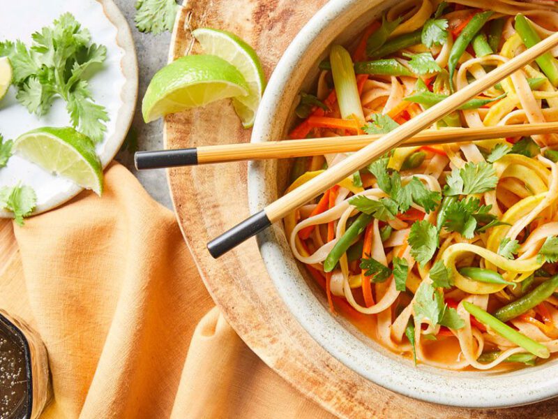 spicy curried thai noodle bowls with chopsticks on a decorative wooden plate