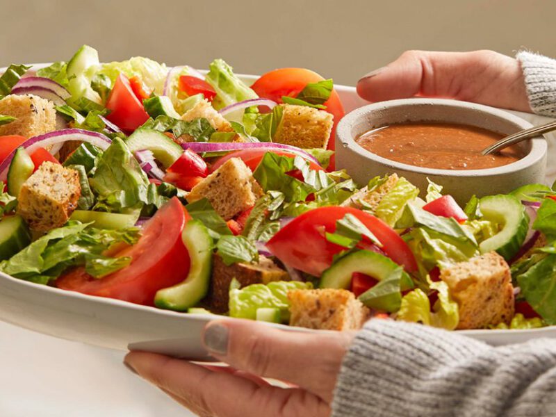 Tuscan Panzanella with Sun-Dried Tomato Vinaigrette on a white platter being held in a woman's arms