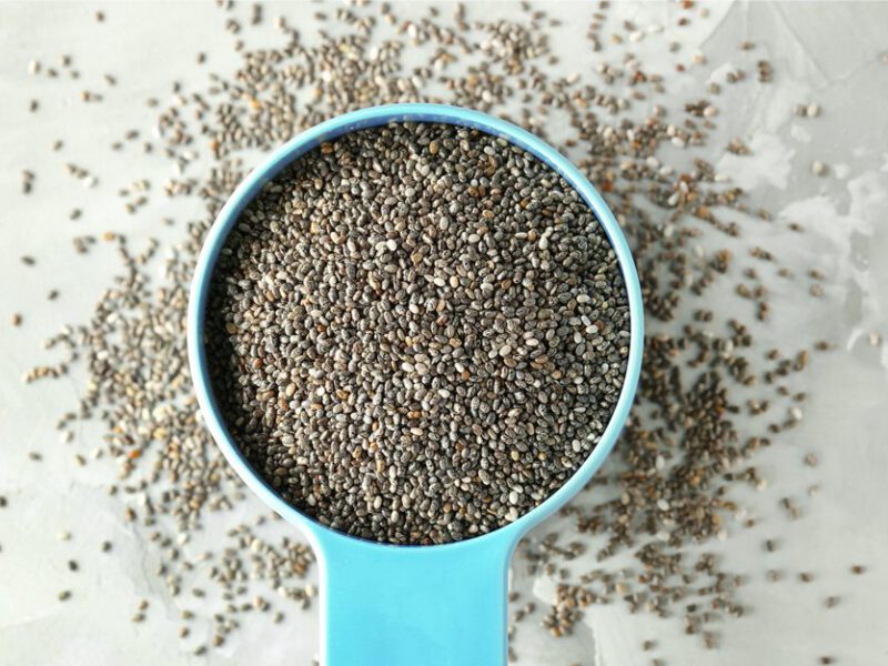 chia seeds in a blue bowl with a handle, with some spilling out underneath and around the bowl onto a gray background