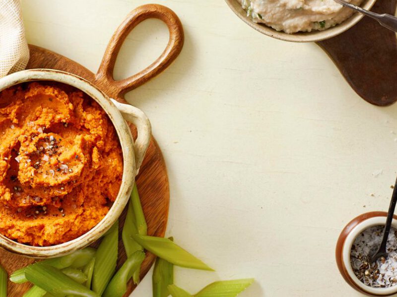 A table with a bowl of harissa roasted hummus, along with edamame and a ramekin of sliced limes