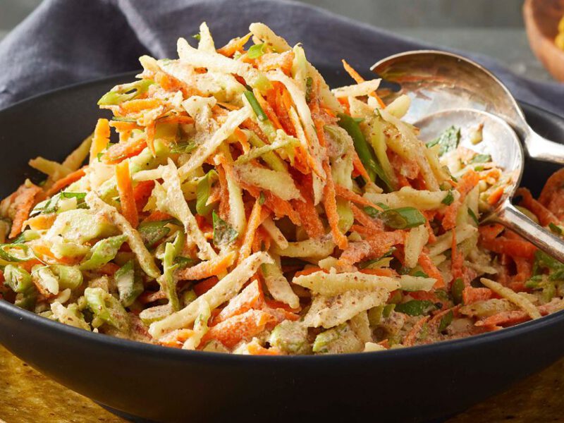 The Best Broccoli Slaw in a black bowl with metal serving spoons