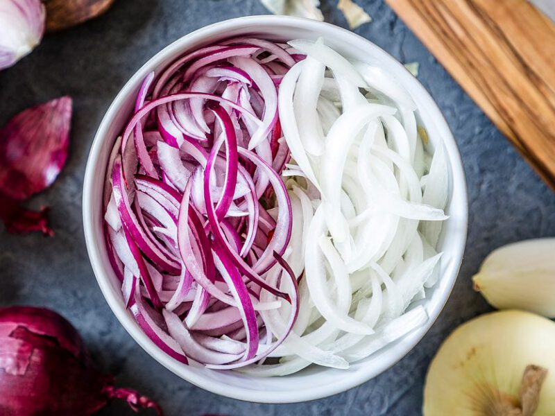 Bowl of sliced red and white onions, with whole red and white onions off to the side