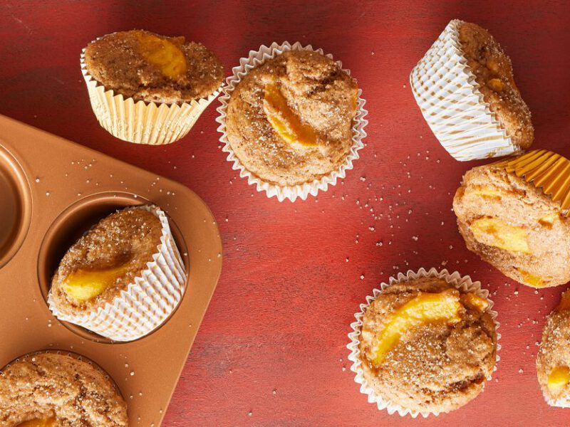 Ginger-Peach Breakfast Muffins on a red table next to a muffin tray