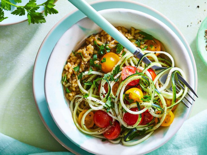 Herbed Vegan Risotto with Zoodles in a white bowl with a metal fork and blue napkin