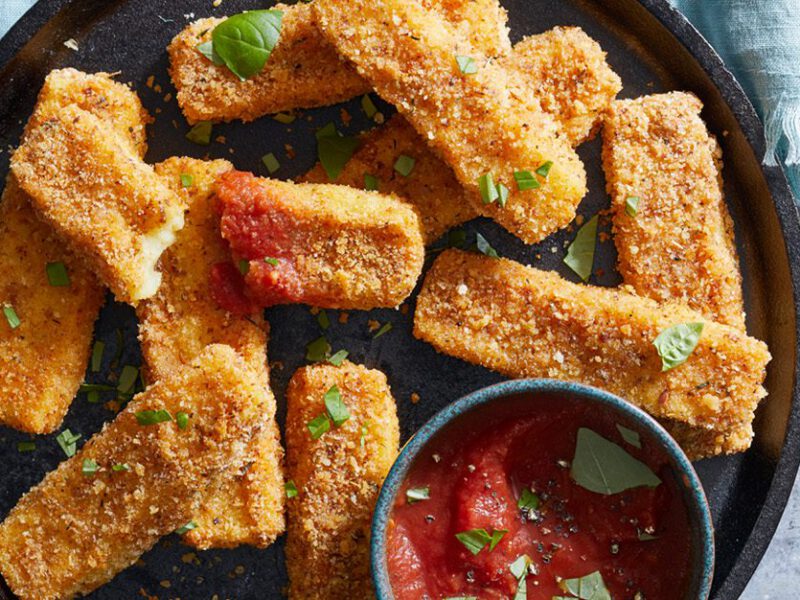 Crispy Potato Vegan Mozzarella Cheese Sticks on a platter with a ramekin of marinara, atop a blue tablecloth