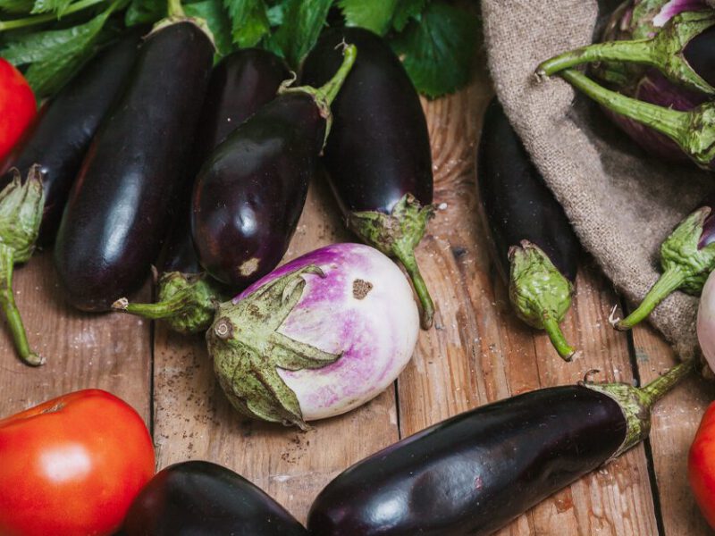 an array of nightshade vegetables -- including eggplant, tomato -- on a wooden table