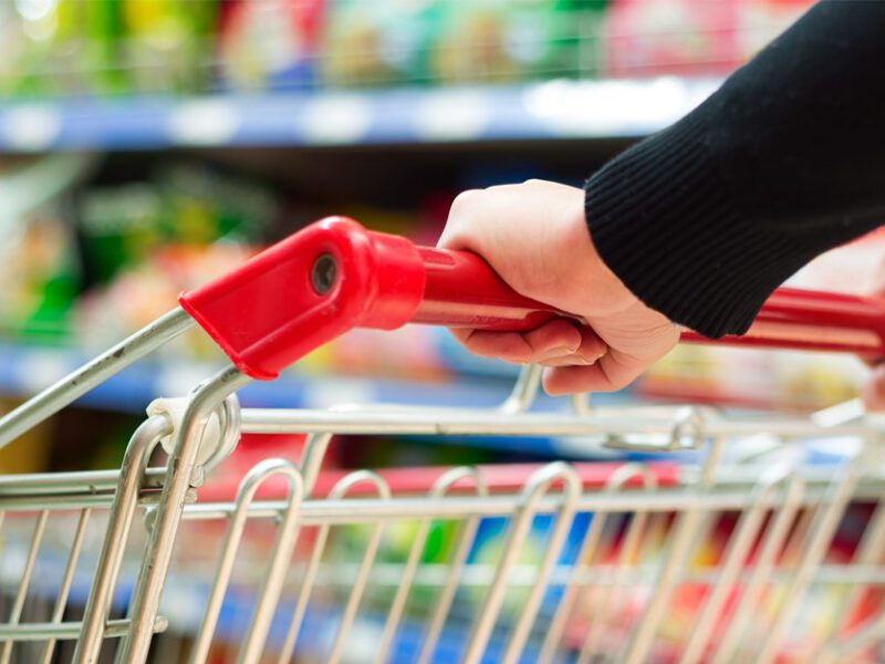 Hands on the red handle of a shopping cart, blurred grocery aisle in the background