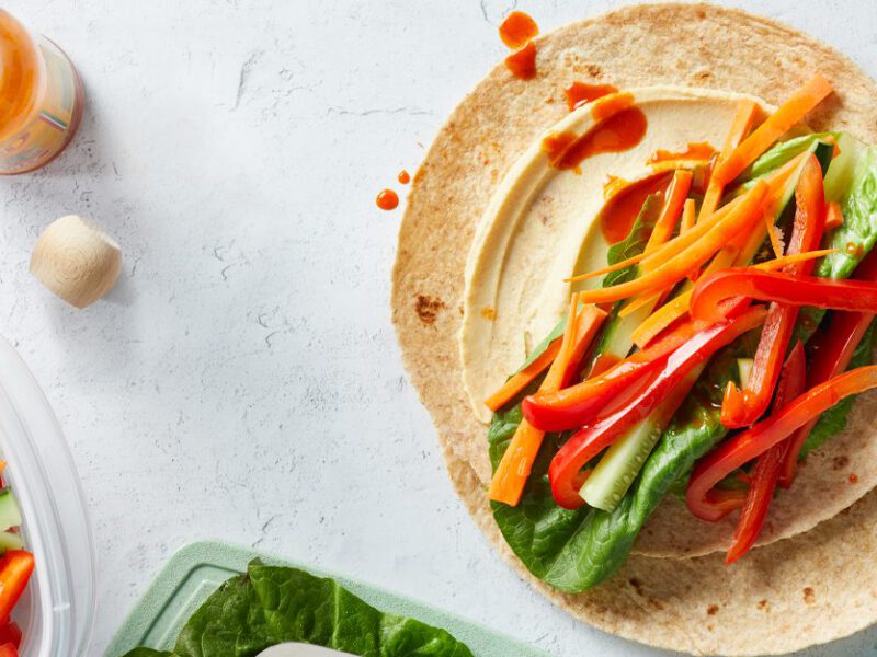 Super-Simple Hummus Veggie Wraps on a white countertop with a bottle of hot sauce