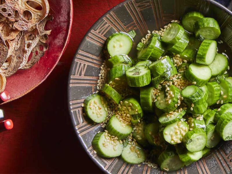 Quick-Pickled Japanese Cucumbers in a ceramic dish on a red table with lotus chips in the corner