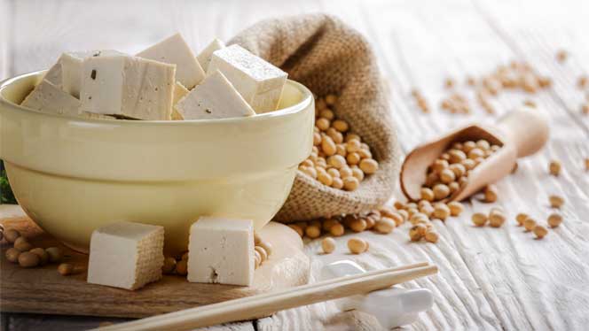 White bowl filled with cubes of tofu surrounded by loose soy beans on a wooden table