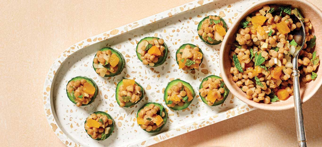 Spiced-Couscous Cucumber Bites on a white ceramic tray with a bowl of extra filling to the right